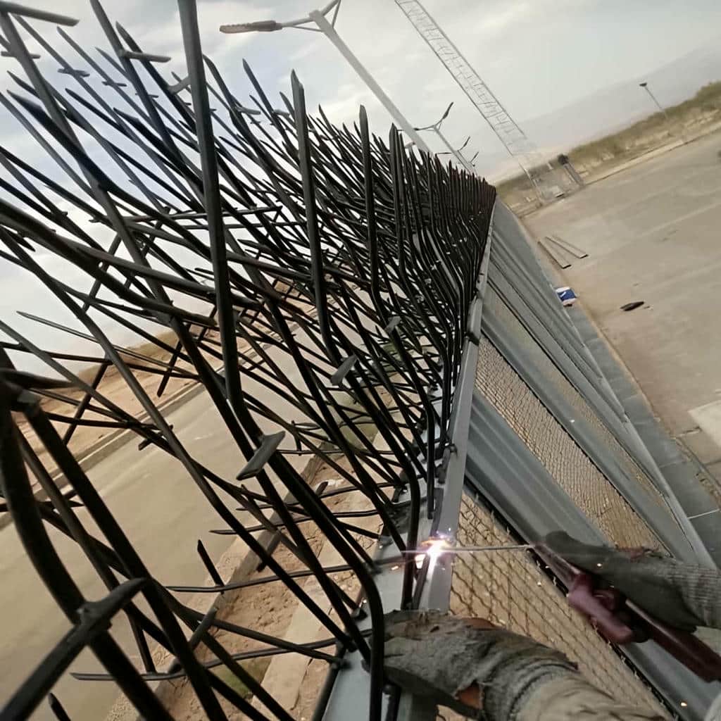 نرده سرنیزه‌ای مشکی روی دیوار سنگی باران‌خورده